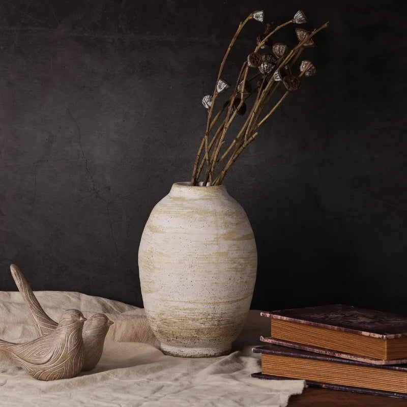Decorative vase with dried flowers on a surface with books and a bird figurine against a dark background